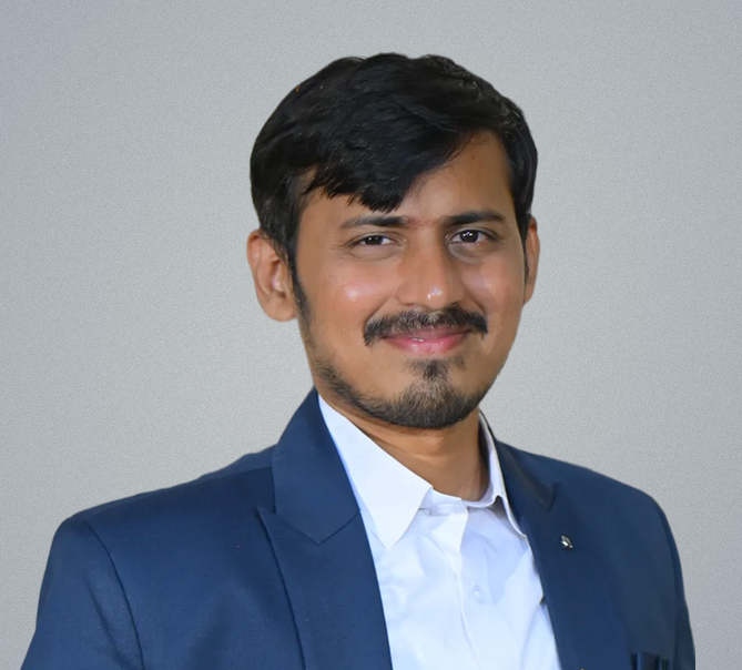 Sravan M, smiling, in a navy jacket over an open-collar white shirt.
